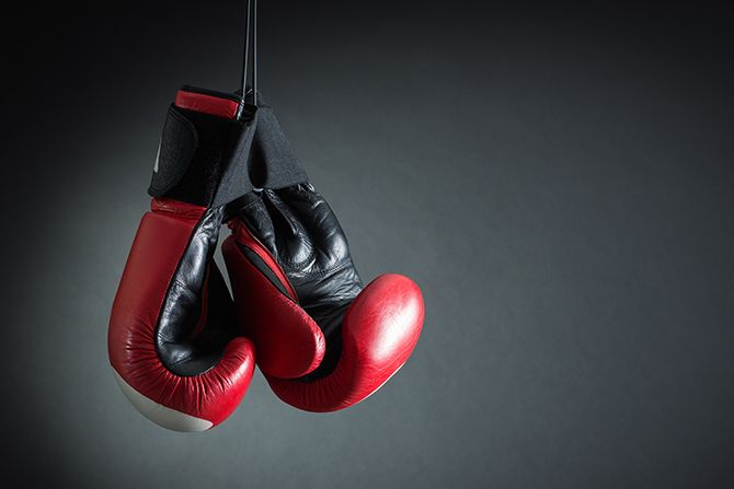 Advocating for You; Red and black boxing gloves hang together against a dark gray background, evoking a sense of readiness and anticipation in a minimalist setting.