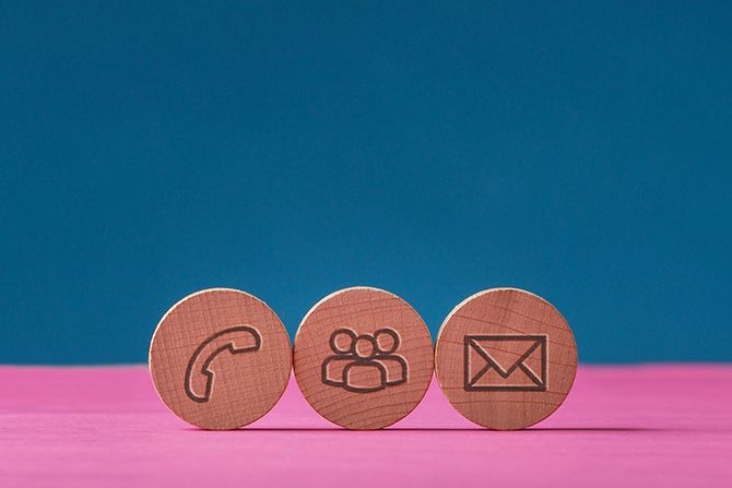 Nebraska Society of CPAs Staff Directory; Wooden discs on a pink surface with blue background, featuring phone, group, and envelope icons, representing communication themes.