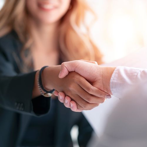 Transformation Trends: Trust Is Still Accounting’s Most Valuable Asset; Two people are shaking hands warmly in a bright setting, symbolizing agreement or partnership. One wears a dark blazer, the other a white shirt.