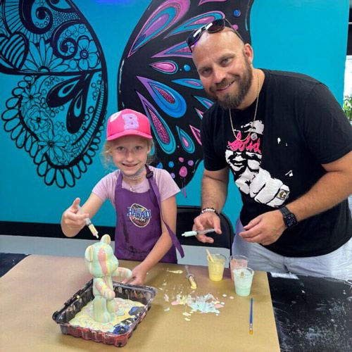 Veteran Finds Opportunity, Work‑Life Balance After Coming Home to Nebraska; A child and an adult, both smiling, are painting a sculpture. They stand in front of a wall with colorful butterfly art, conveying a joyful, creative atmosphere.