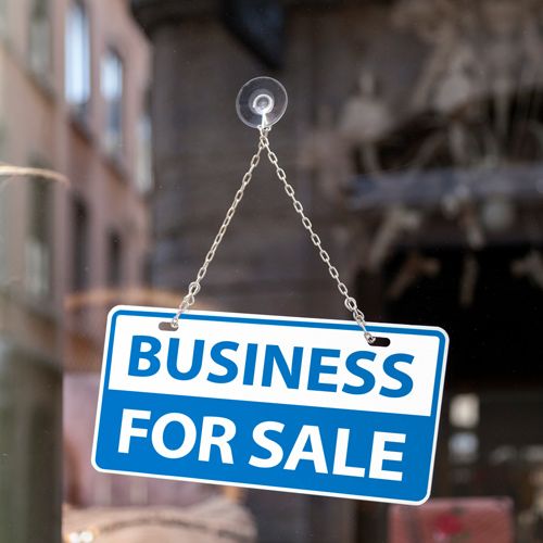 Why Accountants Attempt to Sell on Their Own; Business for Sale sign in bold blue and white hangs on a shop window, reflecting an urban street scene. The tone suggests opportunity and transition.